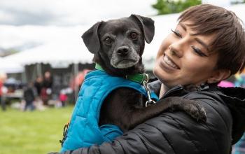 Woman with brown hair in black coat holding black dog in blue coat