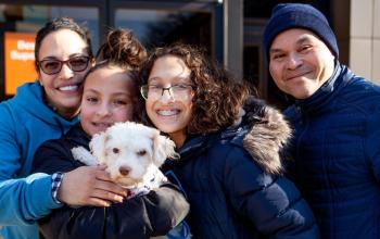 A family of four people holds a small white dog at an adoption event
