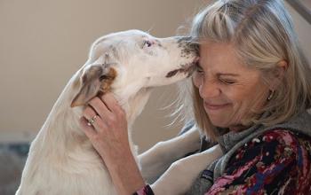 Light colored dog licking the face of a woman