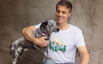 Smiling person sitting outside with a dog against a cement wall