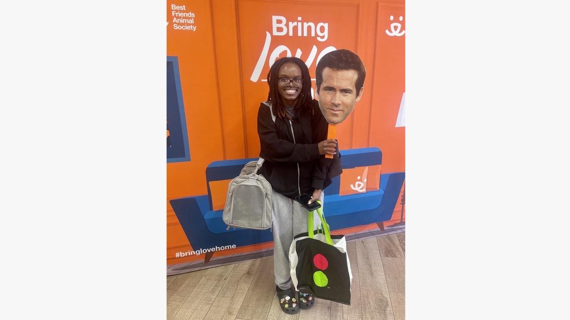 Person holding a Ryan Reynolds face on a stick with the cat carrier holding the cat she'd adopted
