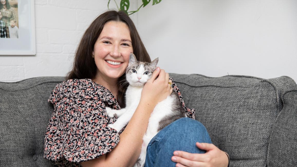 Person sitting on a couch and hugging the cat she adopted