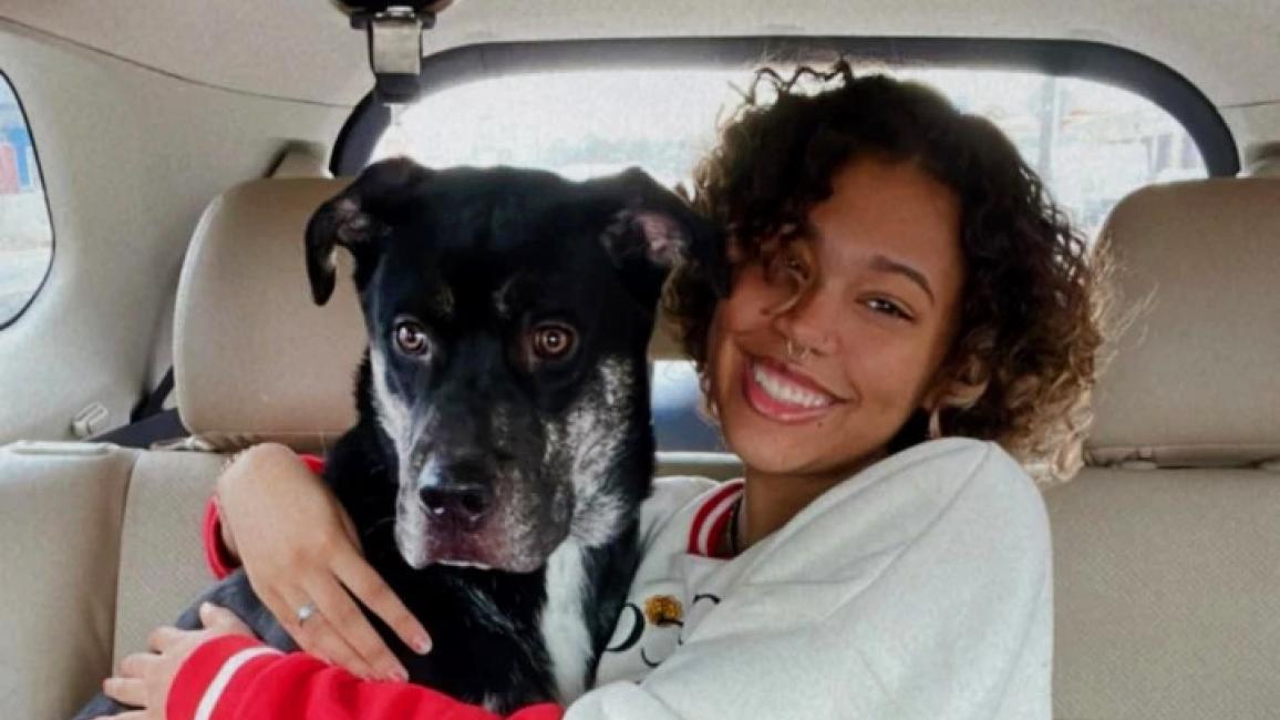 Theo the dog with his smiling adopter hugging him in the back seat of a vehicle