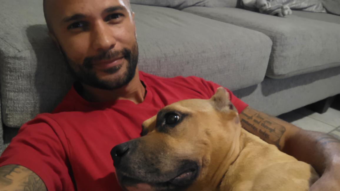 Alex Contreras hugging a brown dog with cropped ears