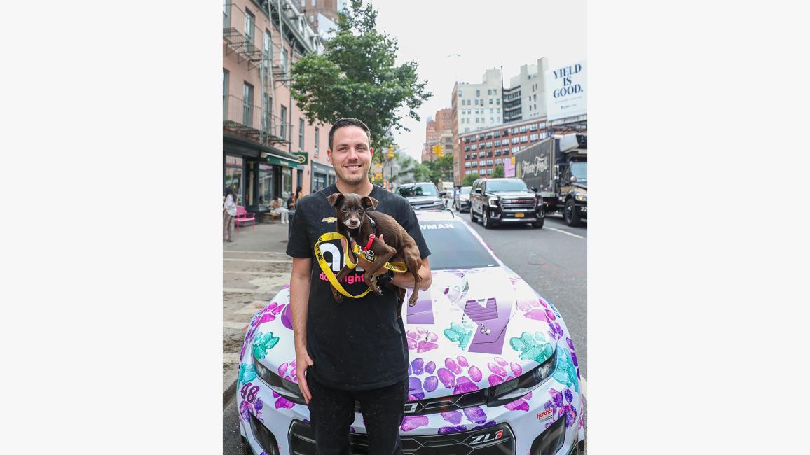 Alex Bowman holding a dog outside the Best Friends Lifesaving Center in New York City in front of his car