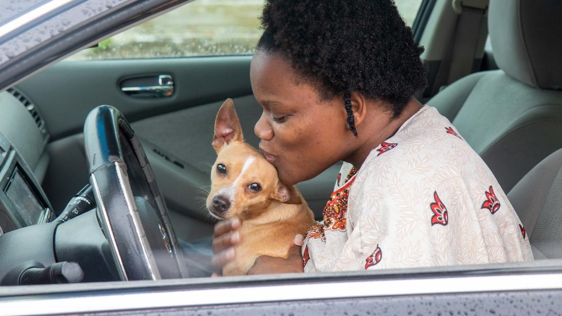 Person kissing a small dog, both in the front seat of a vehicle