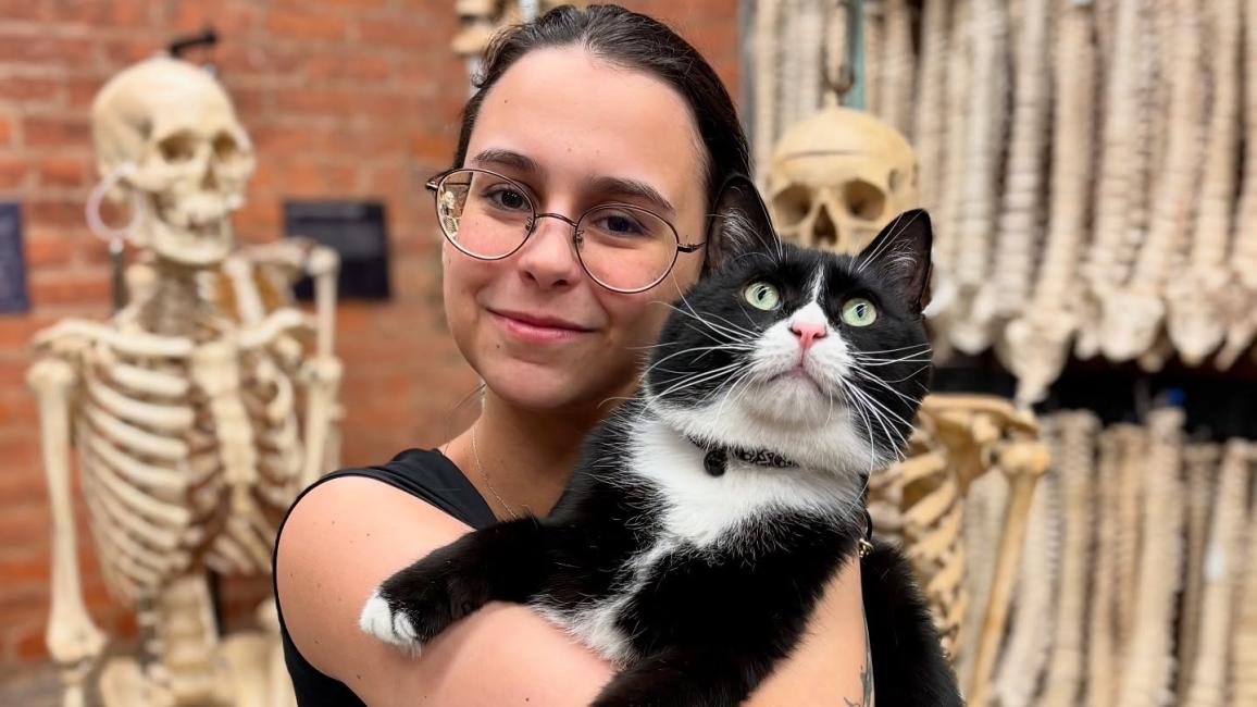 Person holding Bone Jovi the cat in front of some human skeletons