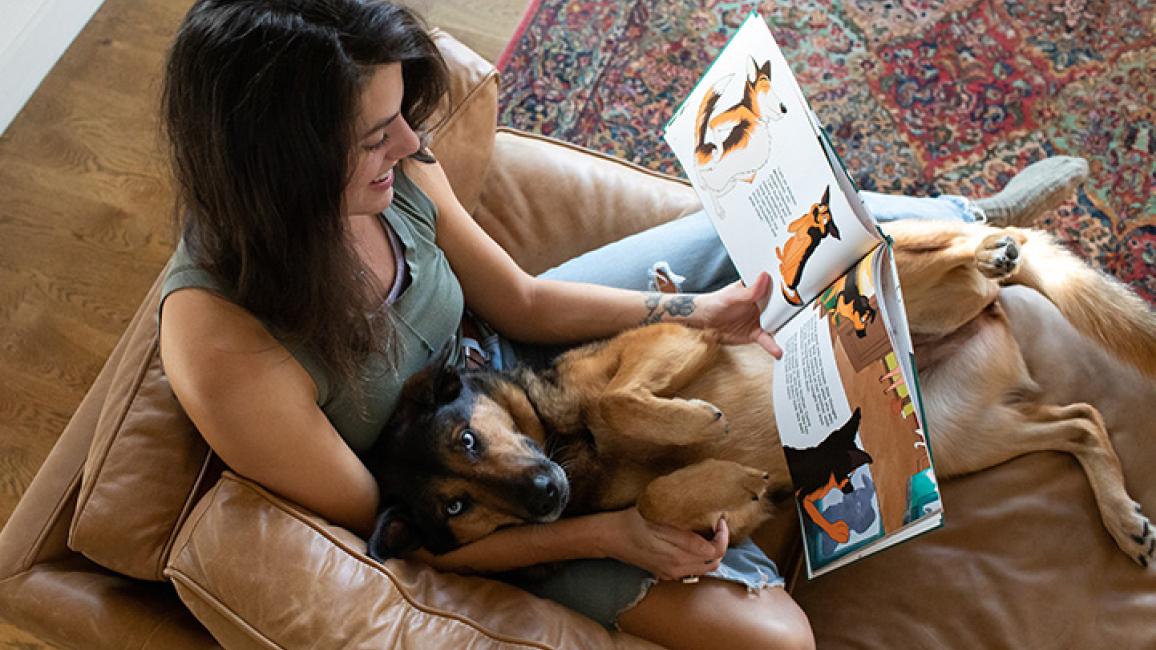 Woman lying on a couch reading a book with dog in her lap