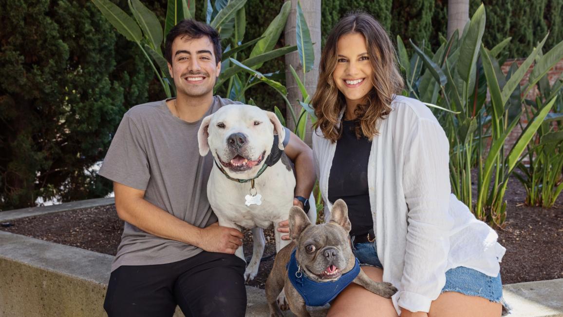 Alyssa Leon and Tommy Rigdon sitting on a ledge with Brew and Julien their adopted dogs