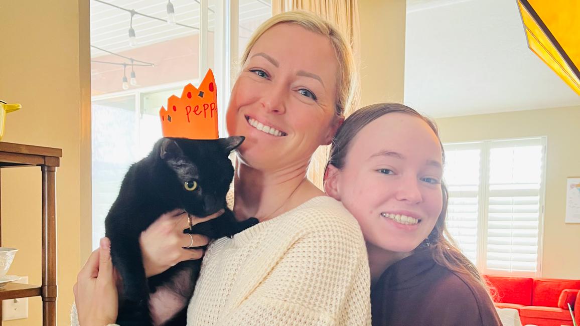Pepper the cat wearing a crown while being held by her new family