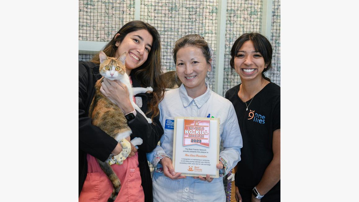 Three happy people posing with a calico cat and a Best Friends no-kill 2023 shelter trophy