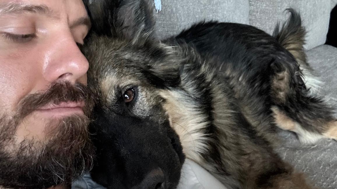 Lars the dog with his new person, lying together on a couch