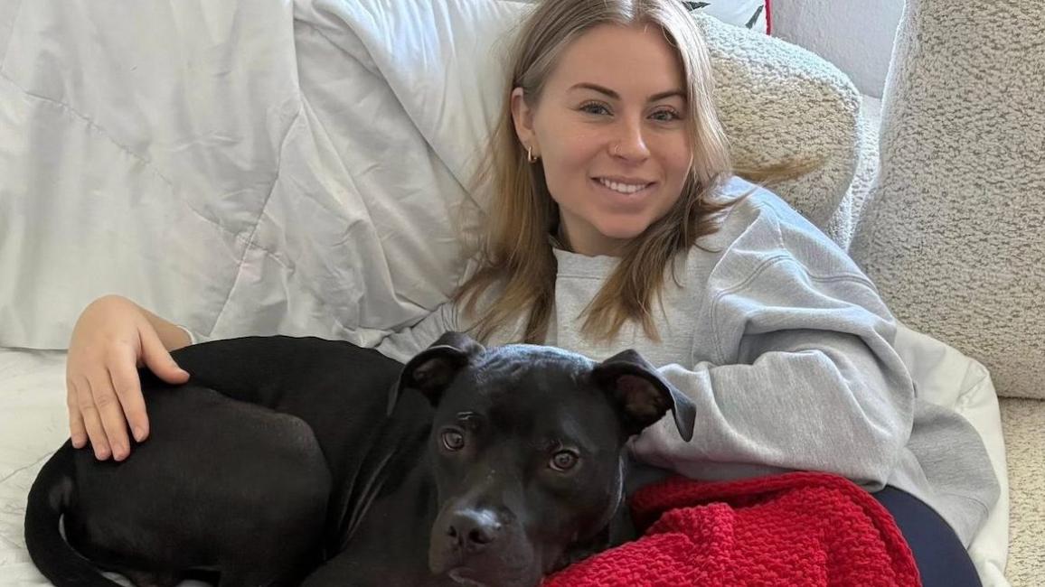 Eli the dog snuggling with Makenna Carew on a bed
