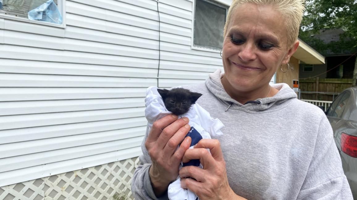 Smiling person holding a small black kitten, next to a mobile home