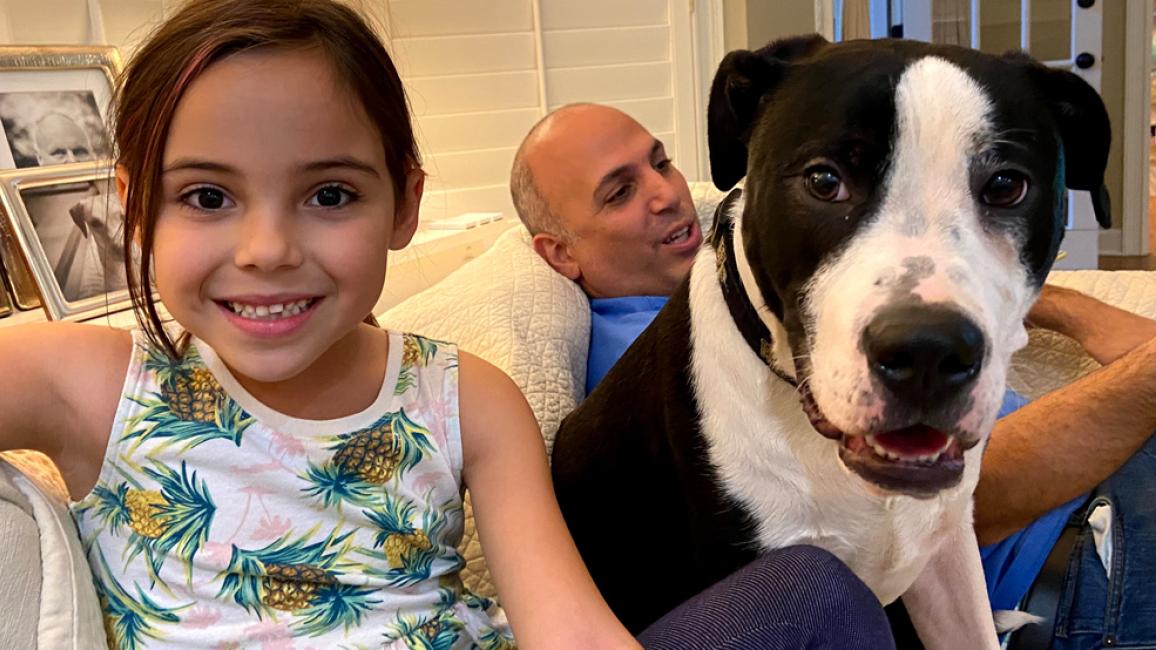 Child smiling and sitting next to black and white dog, with person behind them