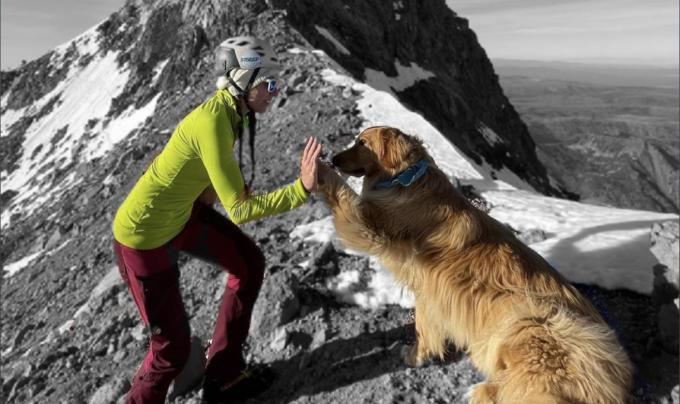 Emily and a dog doing a high-five with a mountain peak behind them