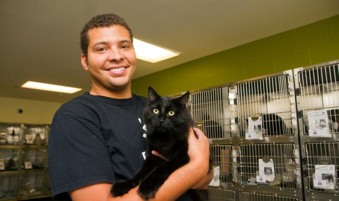 Lawrence Nicolas holding a cat in front of kennels