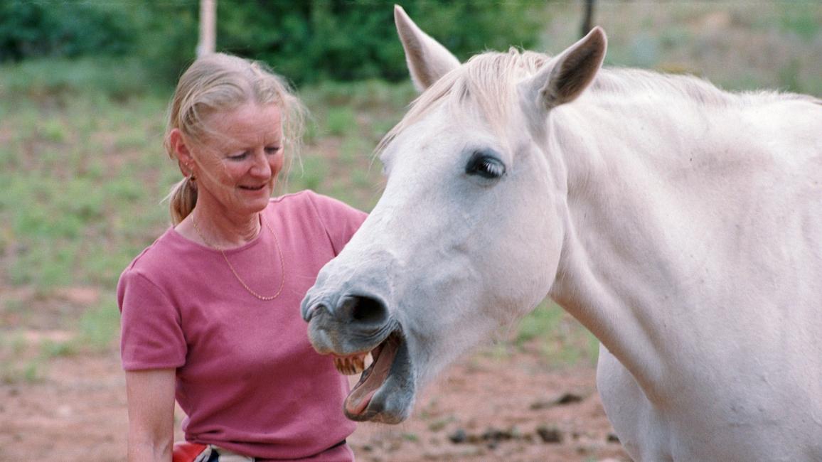 Best Friends Animal Society co-founder Diana Asher outside with a white horse whose mouth is open