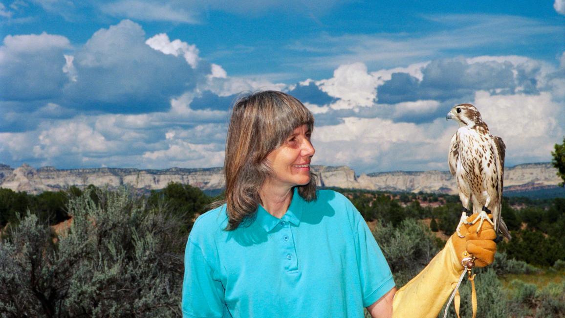 Vintage photo of Sharon St. Joan holding a bird of prey with cliffs and a beautiful sky in the background