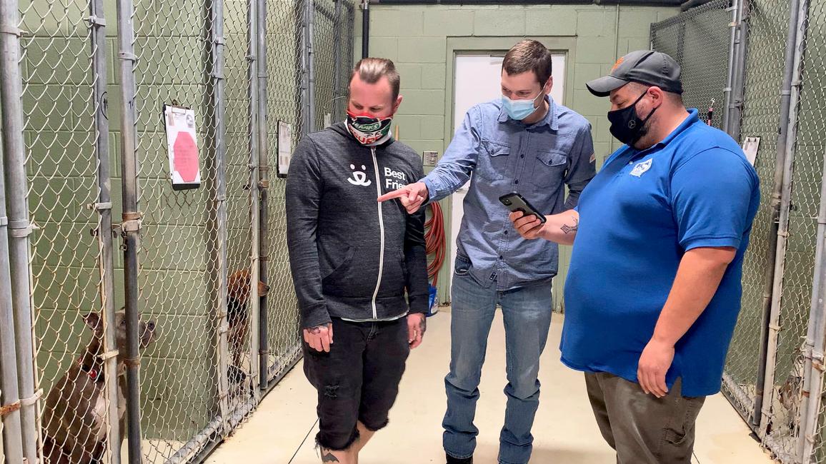 Three people from Horry County Animal Care Center and Best Friends in a dog kennel, with one person pointing