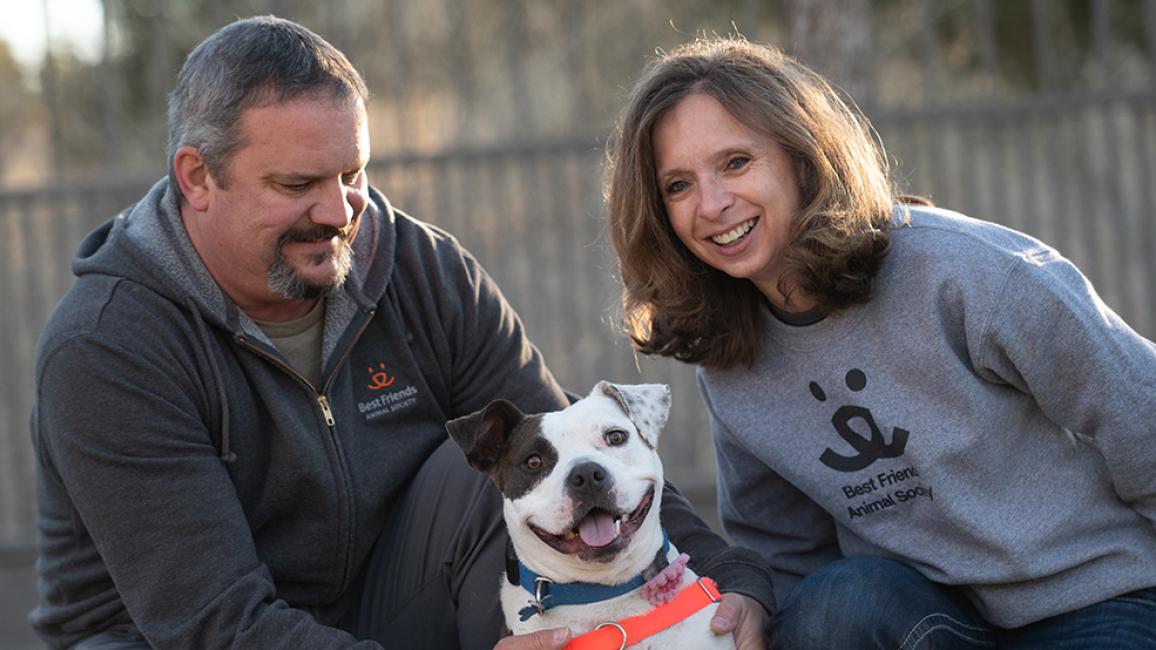Bella the dog, smiling, between the two people who adopted her