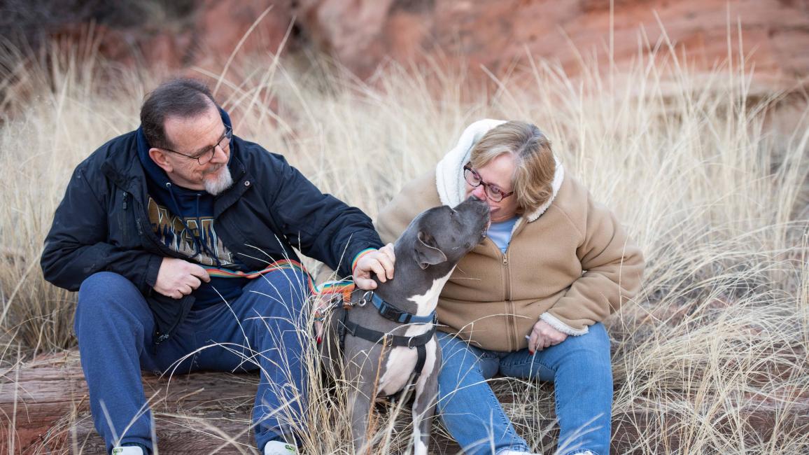Jessa the dog with her adopters outside in some dried grass