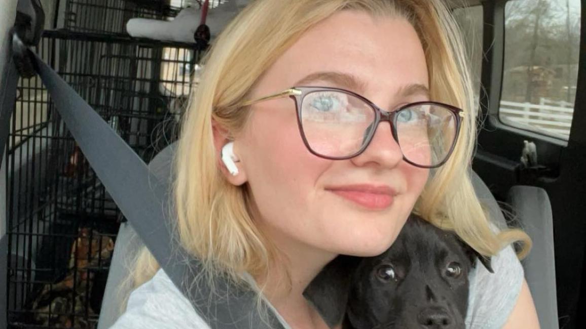 Emily Hirtle in a vehicle holding a small black puppy with a gloved hand