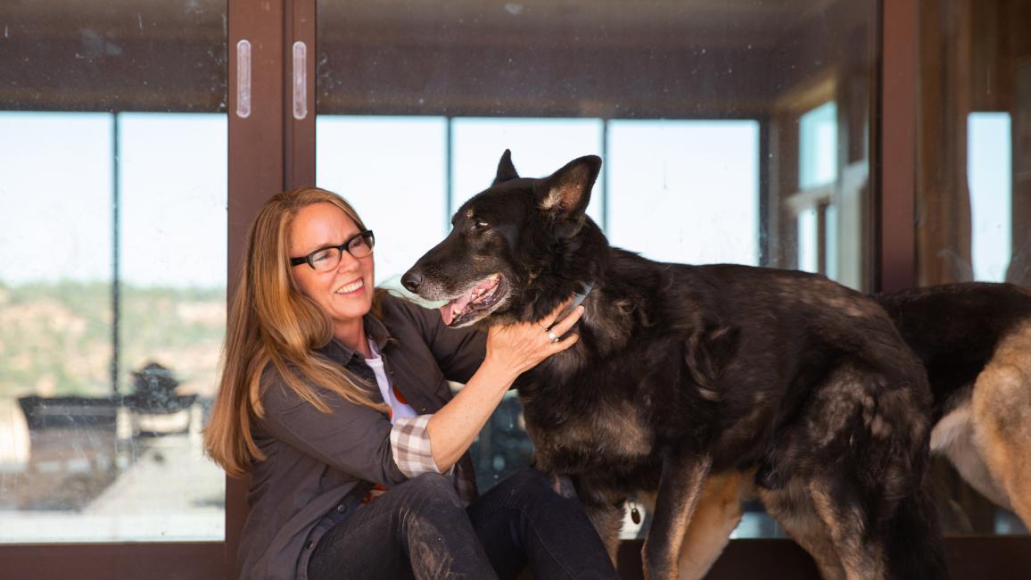 Best Friends CEO Julie Castle with her dog Shadow in front of a large window