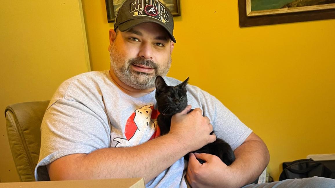 Kelly Burkhart holding Trinna the black kitten in front of a yellow wall