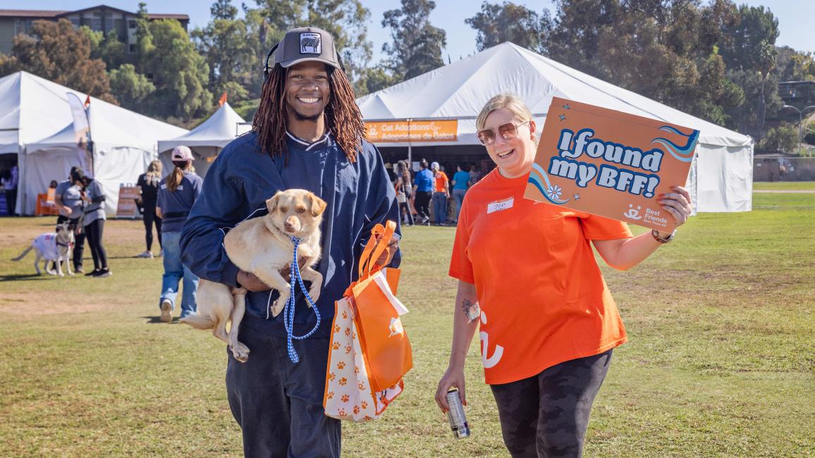 Person carrying a puppy beside a Best Friends volunteer holding a sign that says, 'I found my BFF'