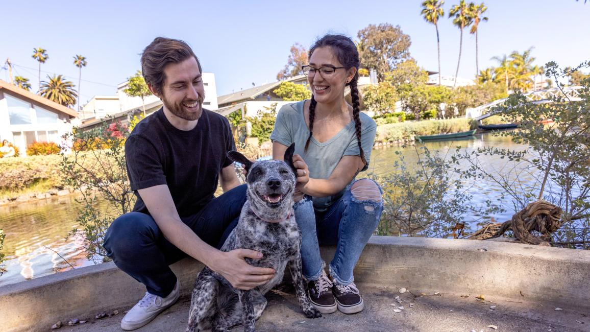 Two people sitting outside with a happy dog between them