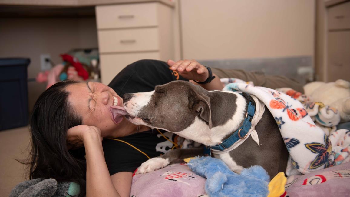 Liz Tran lying beside Sage the dog, who is licking her face