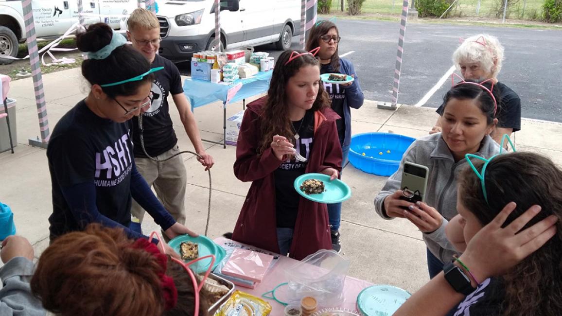 Group of people celebrating outside, one eating cat and multiple wearing cat ears