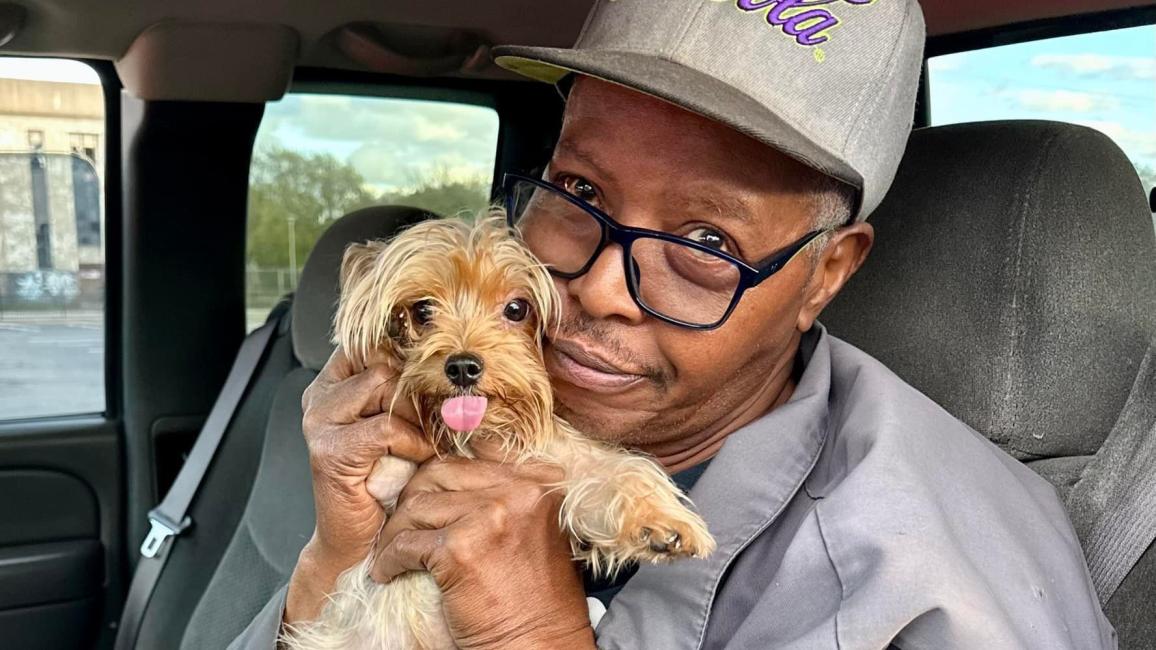 Person hugging a small dog in the driver's seat of a car