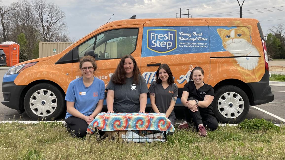Four people in front of a Fresh Step branded van with a live trap covered with tie-die material