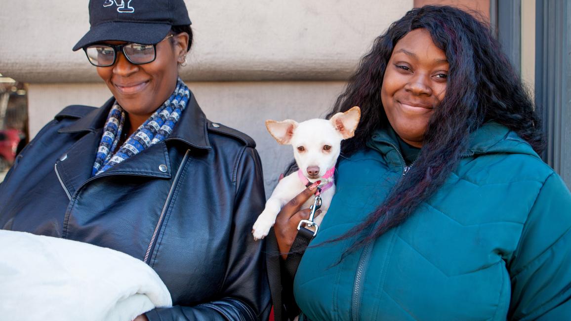Two smiling people holding a small white dog