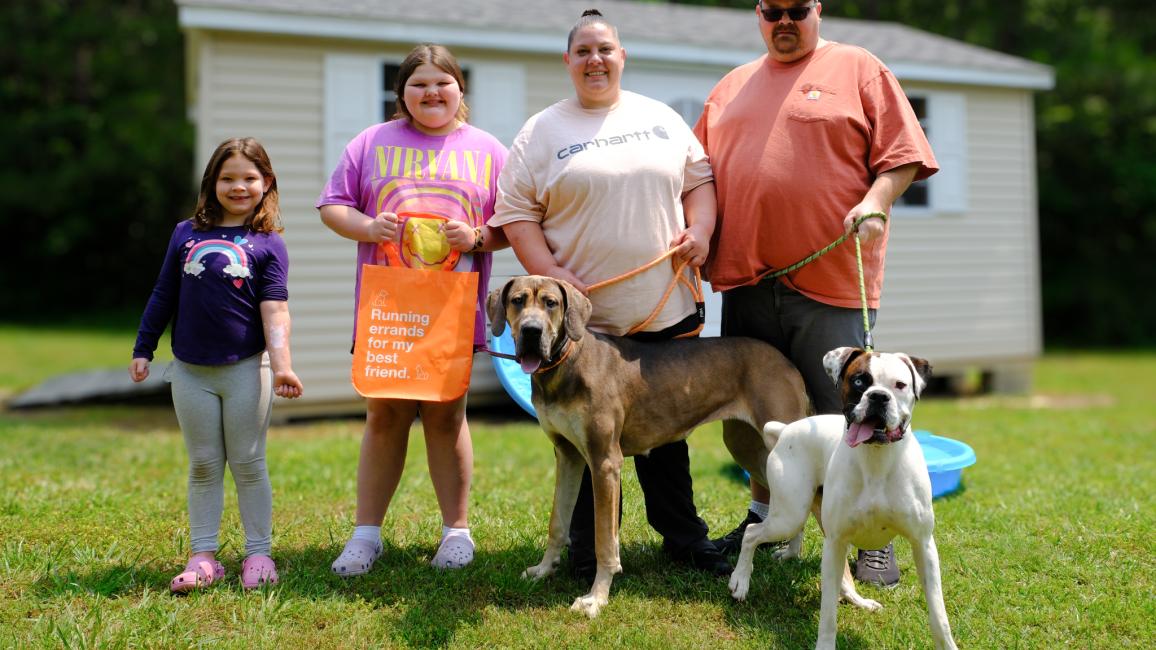 Four people with two dogs on leashes in front of a shed