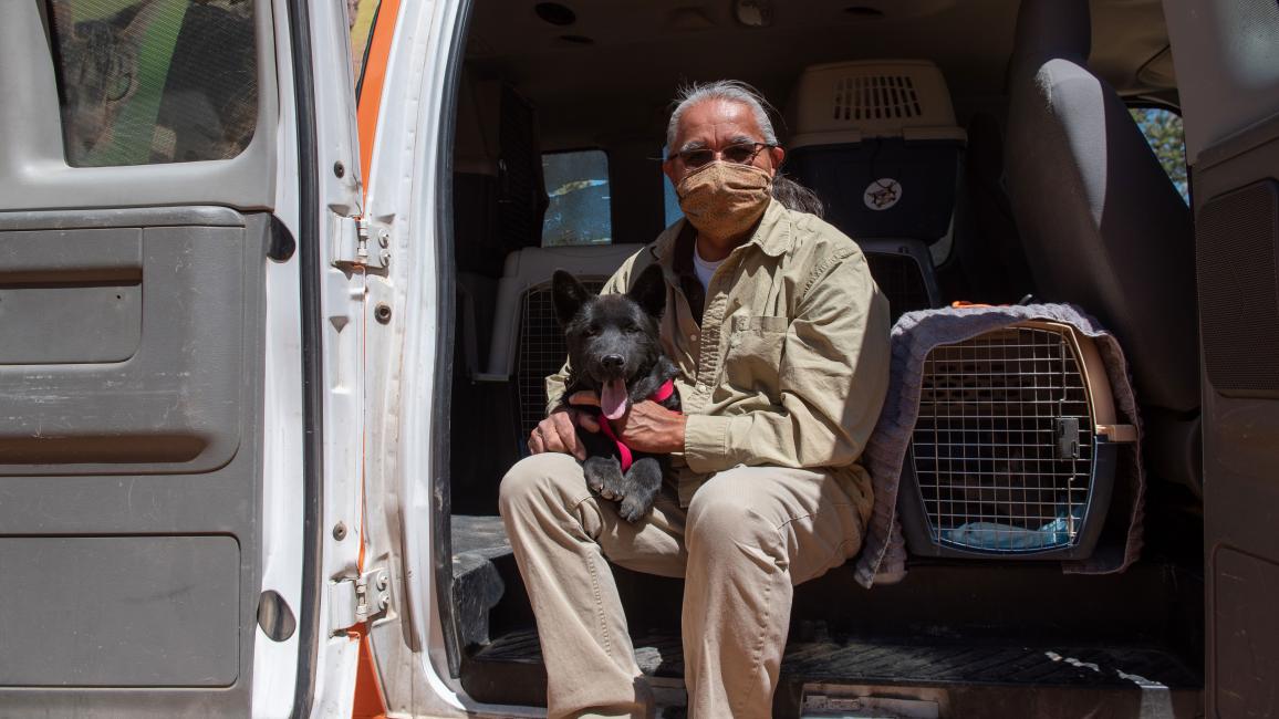 Keith Slim-Tolagai with a dog on his lap, sitting in the open door of a transport van