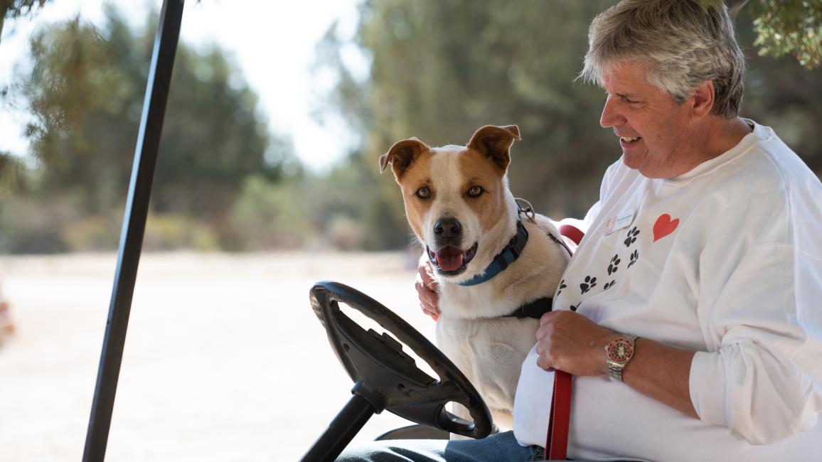 Caregiver Tim Dempsey in a golf cart with Abbott the dog