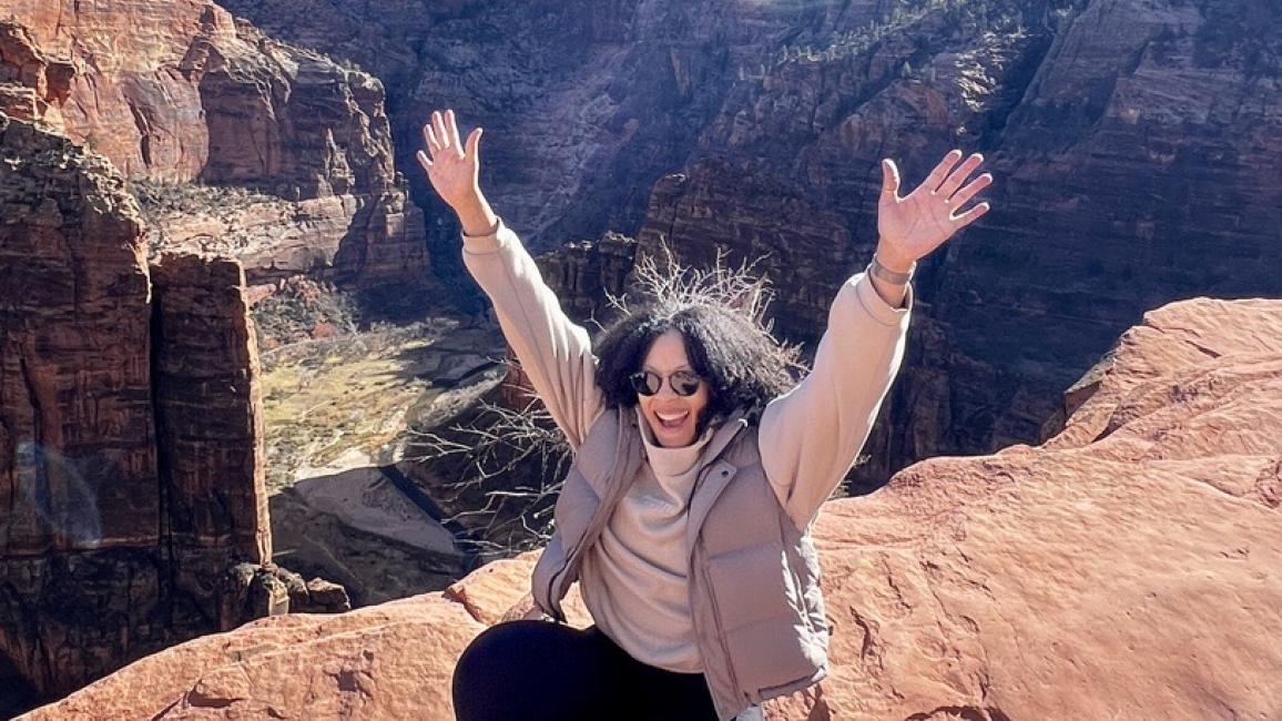 Tara Pope on a rock cliff with arms outstretched