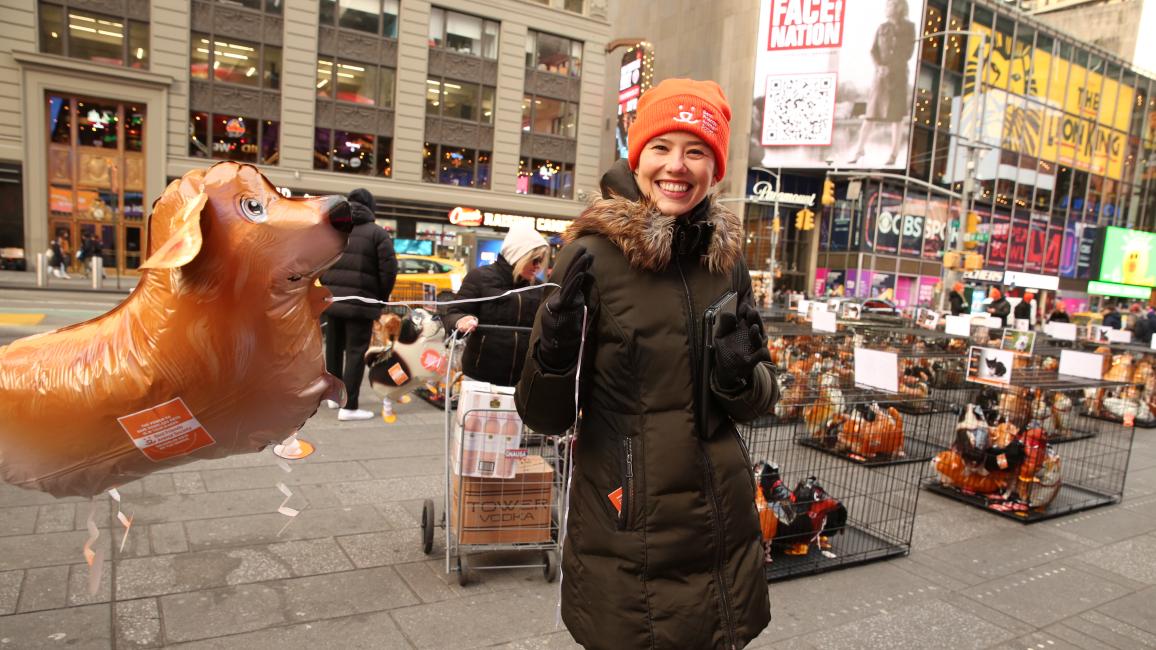Smiling person wearing an orange Best Friends hat holding a dog balloon in Times Square