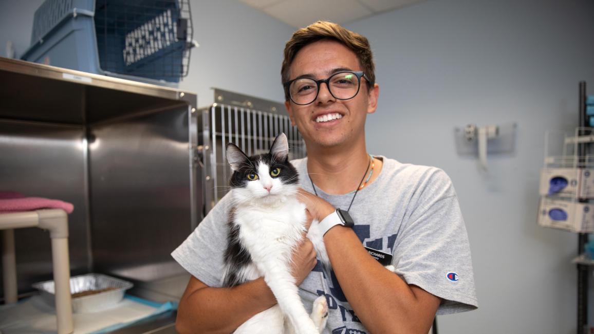 Volunteer Ben Richards holding a black and white cat in front of some kennels