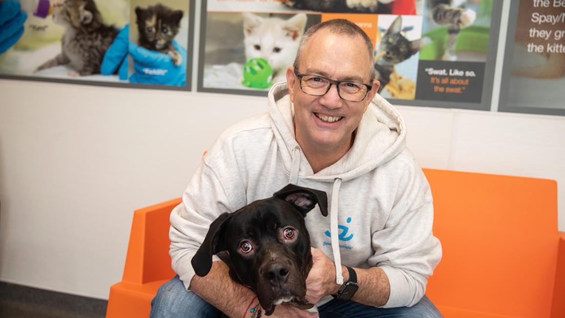 Volunteer Jeff Harris sitting on an orange seat hugging a black and white dog in front of him