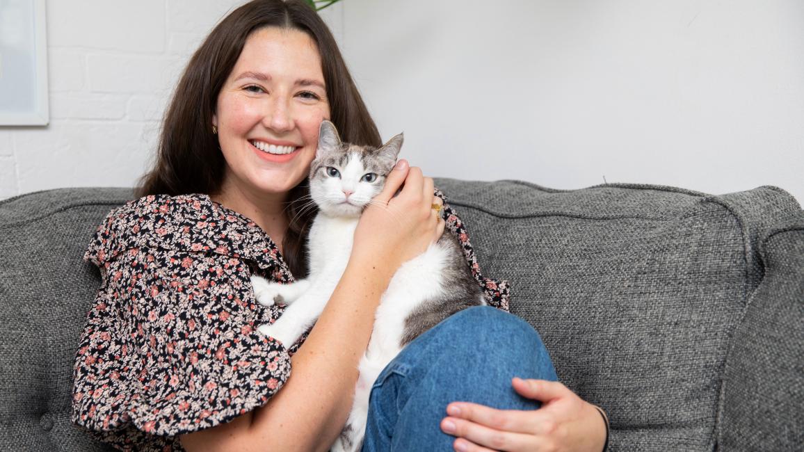 Smiling person sitting on a couch while holding a cat