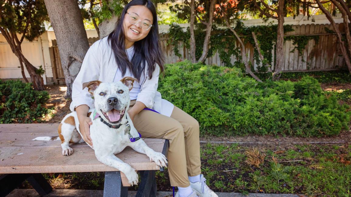 Shannon sitting on an outdoor table next to Felix the dog, both of them smiling