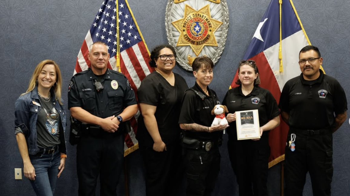 Bedford Animal Shelter staff in front of an American and Texas flag holding a Best Friends award and stuffed dog