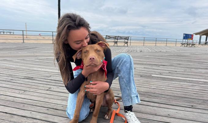 Masha kissing Cinnamon the dog on a boardwalk