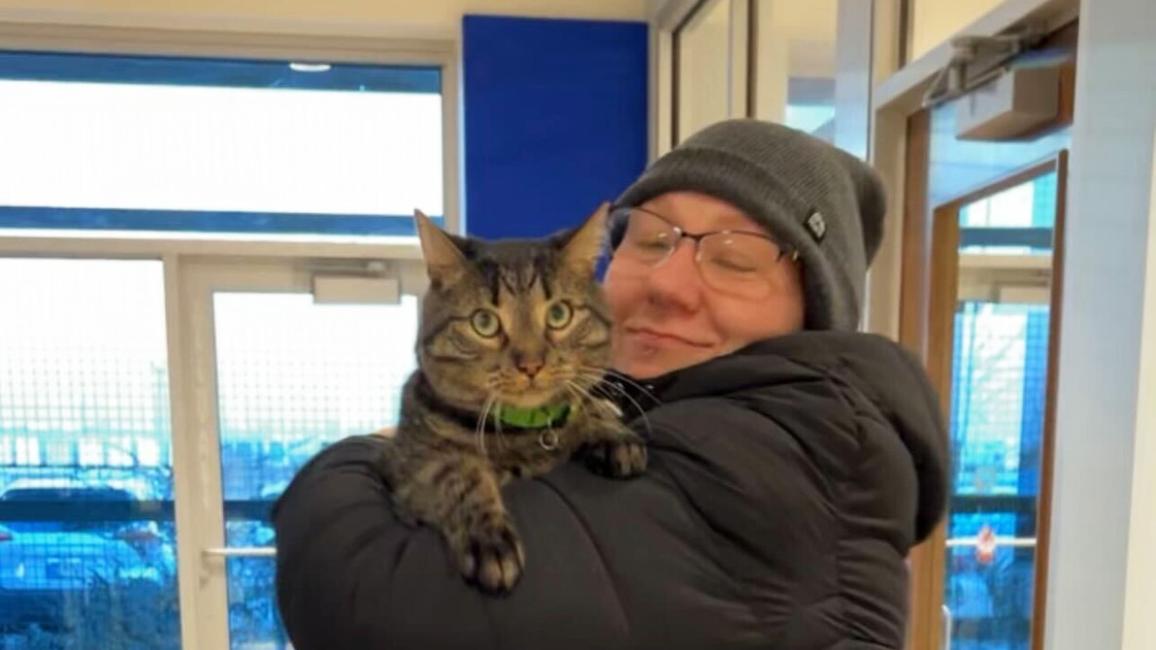 Smiling person wearing winter clothing happily hugging a tabby cat