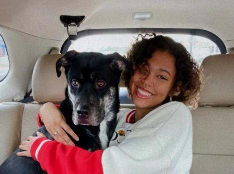 Theo the dog with his smiling adopter hugging him in the back seat of a vehicle