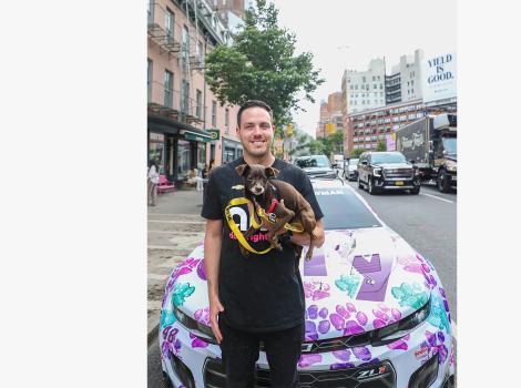 Alex Bowman holding a dog outside the Best Friends Lifesaving Center in New York City in front of his car